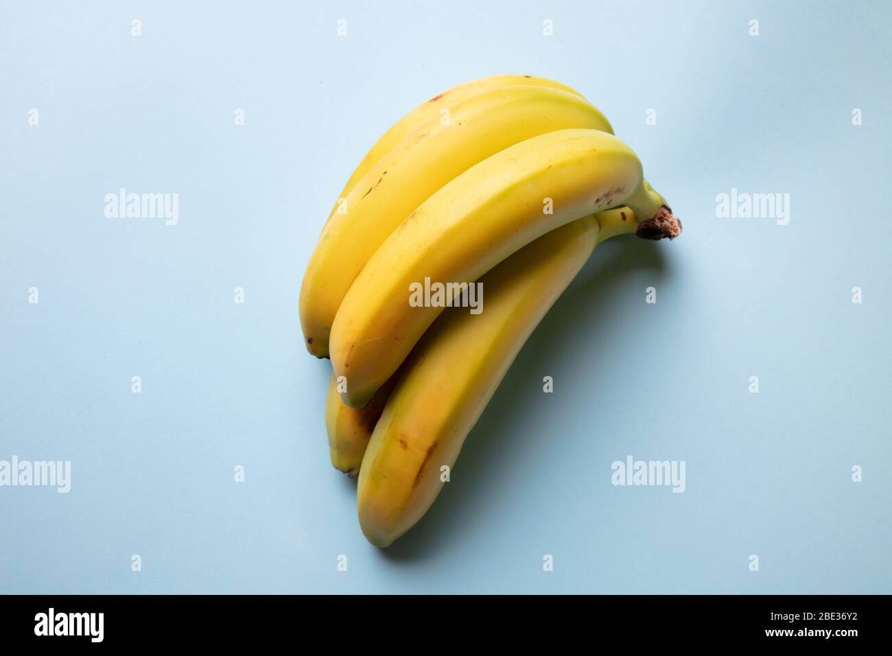 a fresh view of a bunch of yellow bananas resting on a pastel light blue background, top view Stock Photo