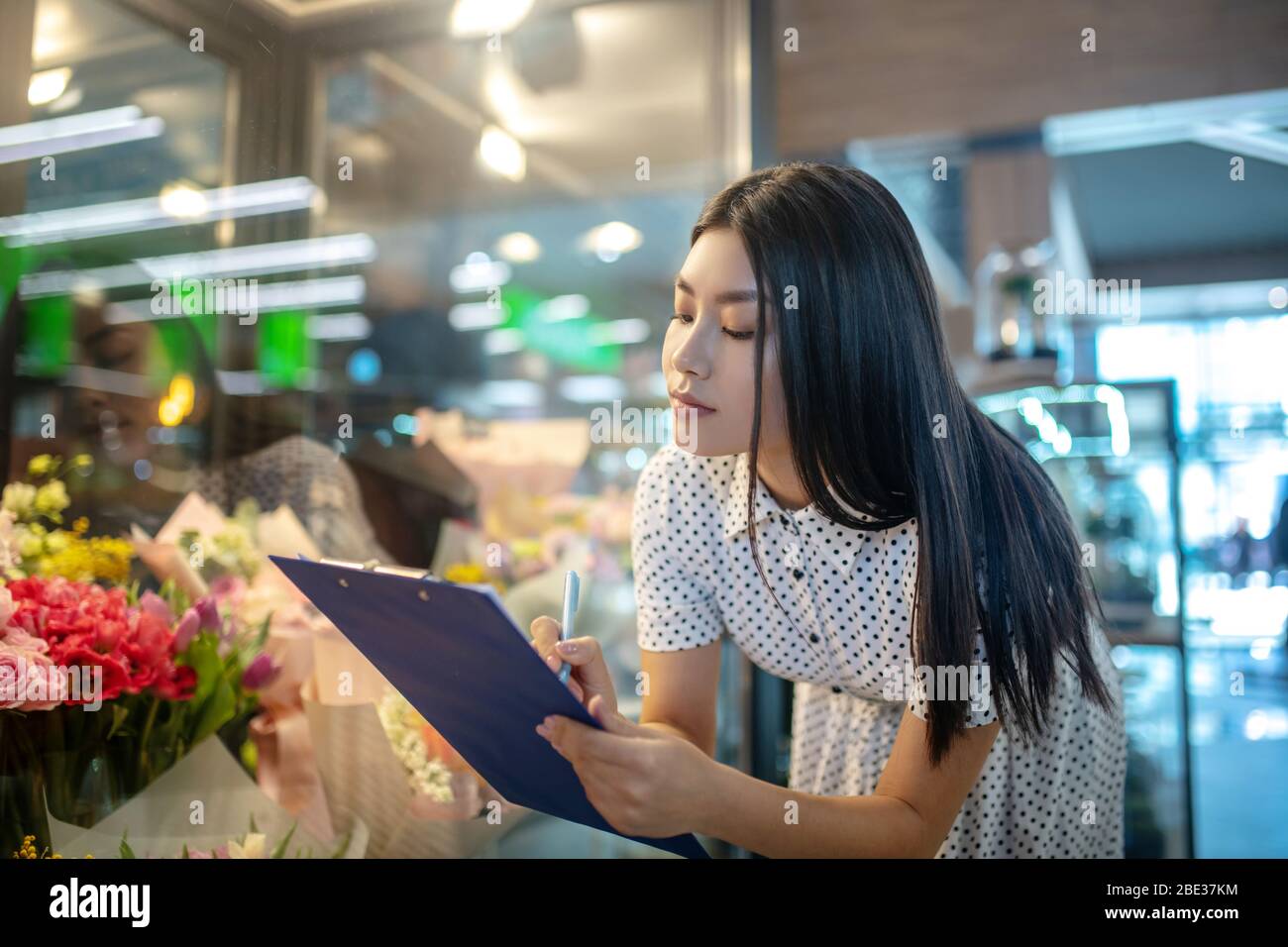 Dark-haired asian flower shop assistant making notes Stock Photo