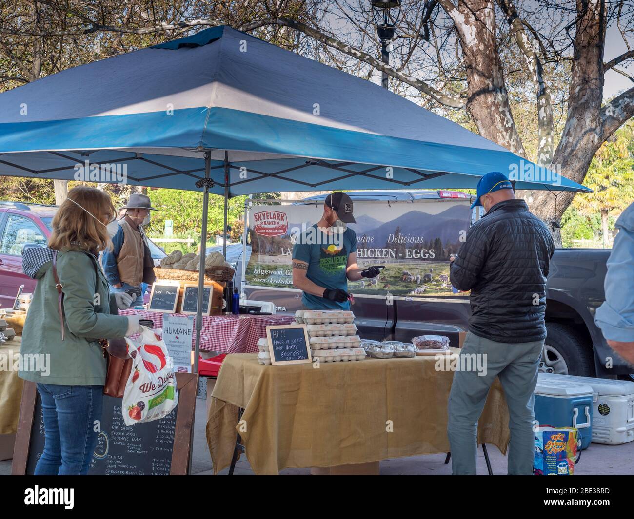 Davis, California, USA. March 11, 2020. The farmers market is still open despite the lockdown. The tents are  more spread out and only the vendors can touch the produce. Money and produce are handled by different people. Hand sanitizer are offered, and lmost everyone is wearing masks (some more fashionable than others). Stock Photo