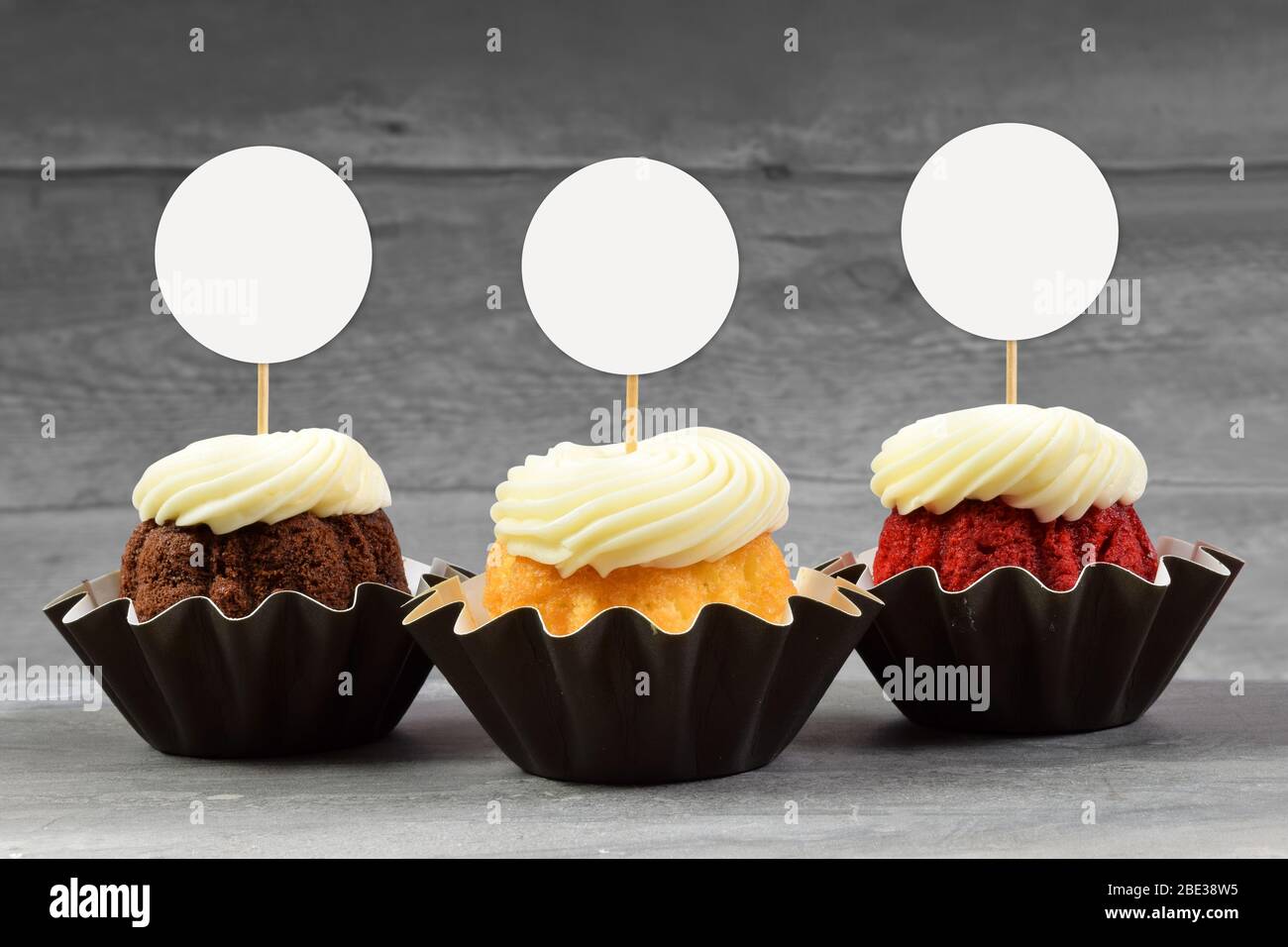 Three tempting gourmet cupcakes atop a gray marble surface with round cupcake toppers Stock