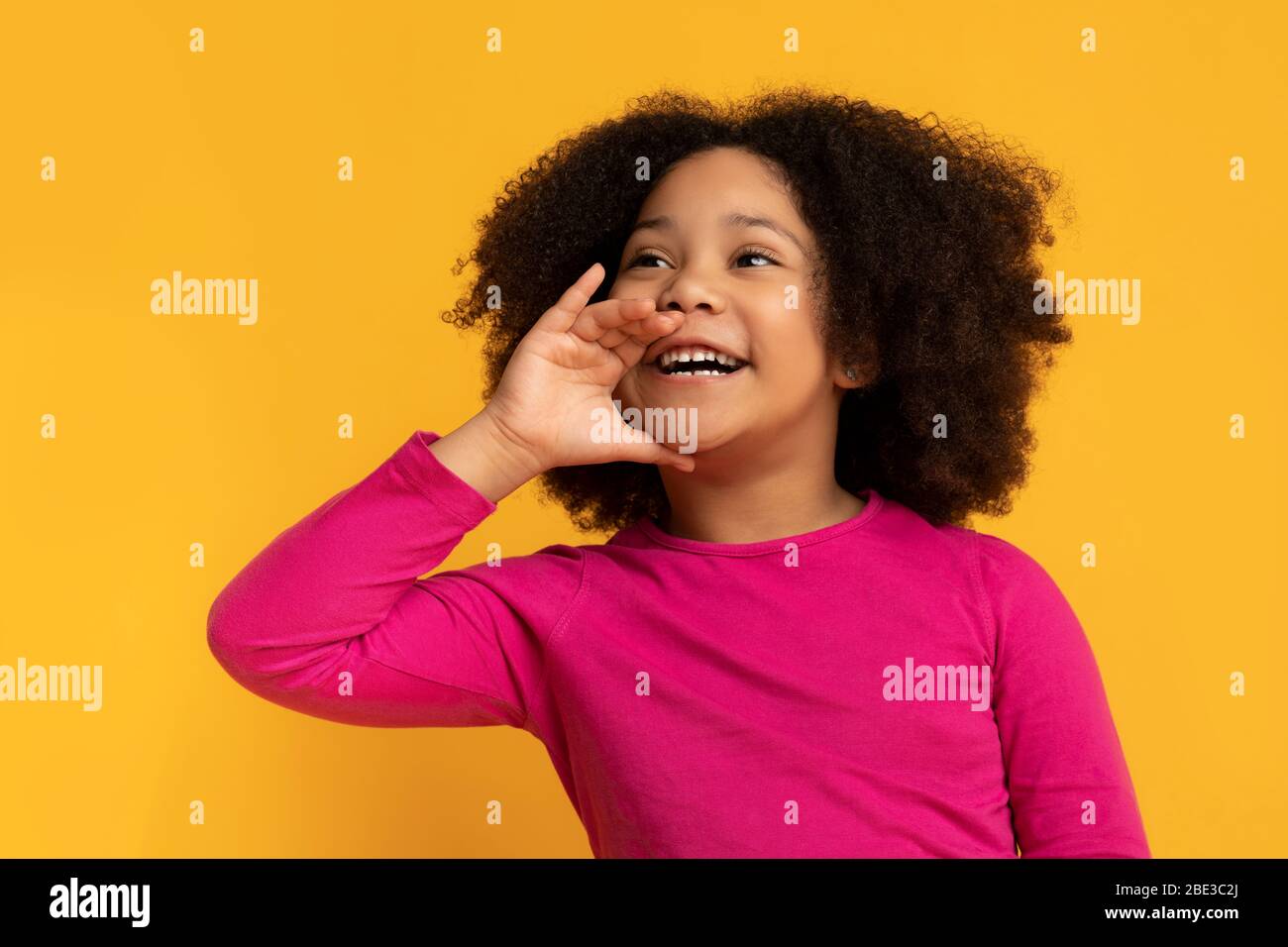 Overjoyed cute little black child holding hand near mouth, making announcement Stock Photo