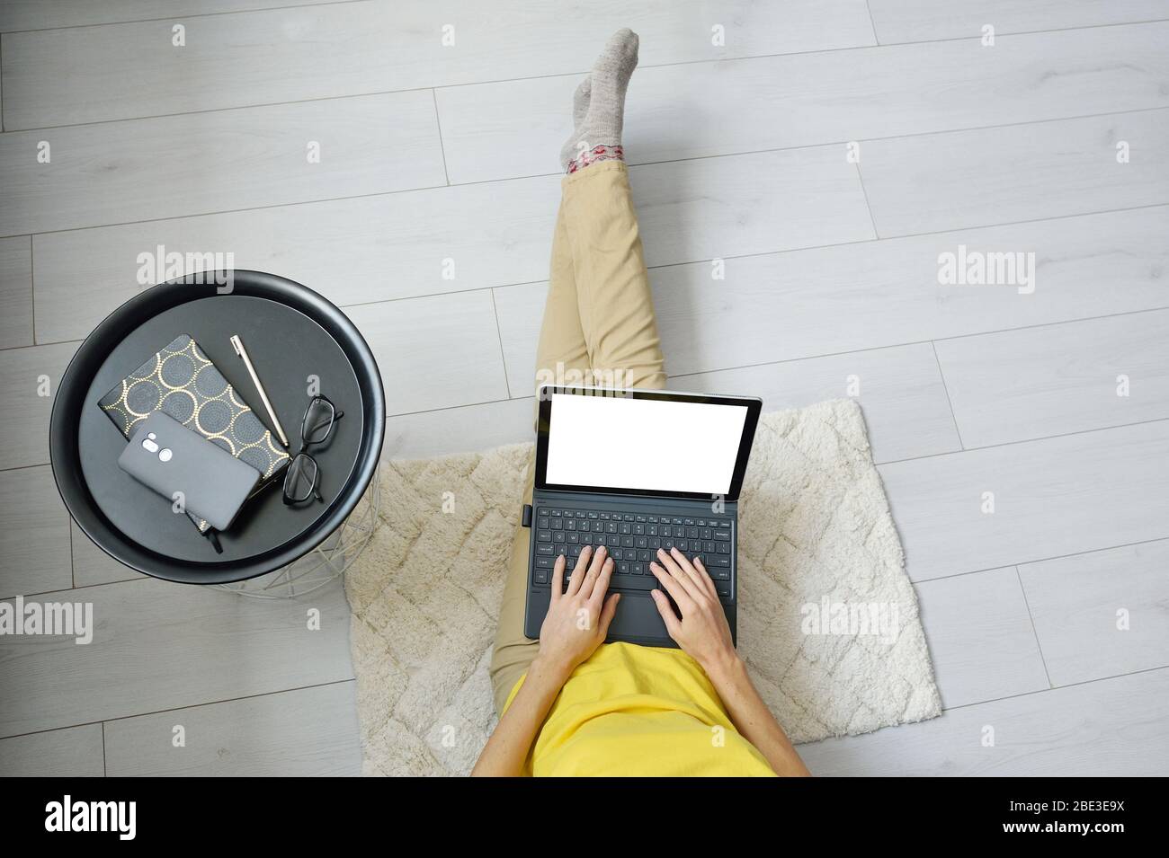 Top view mockup of female freelancer sitting on floor near sofa at home stay and working on laptop computer. Woman typing on laptop. quarantine Stock Photo