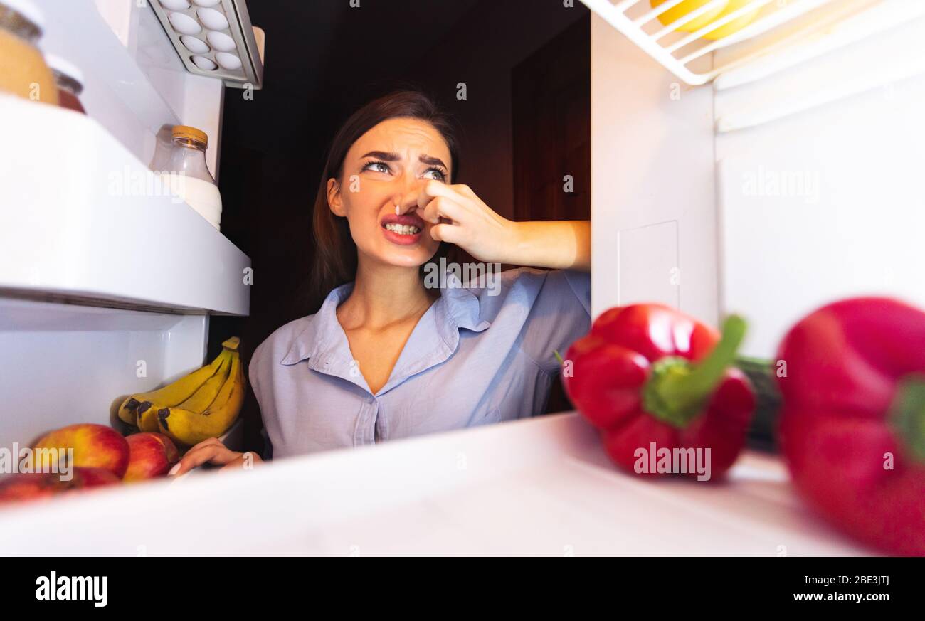 Woman closing nose near refrigerator, feeling bad smell Stock Photo