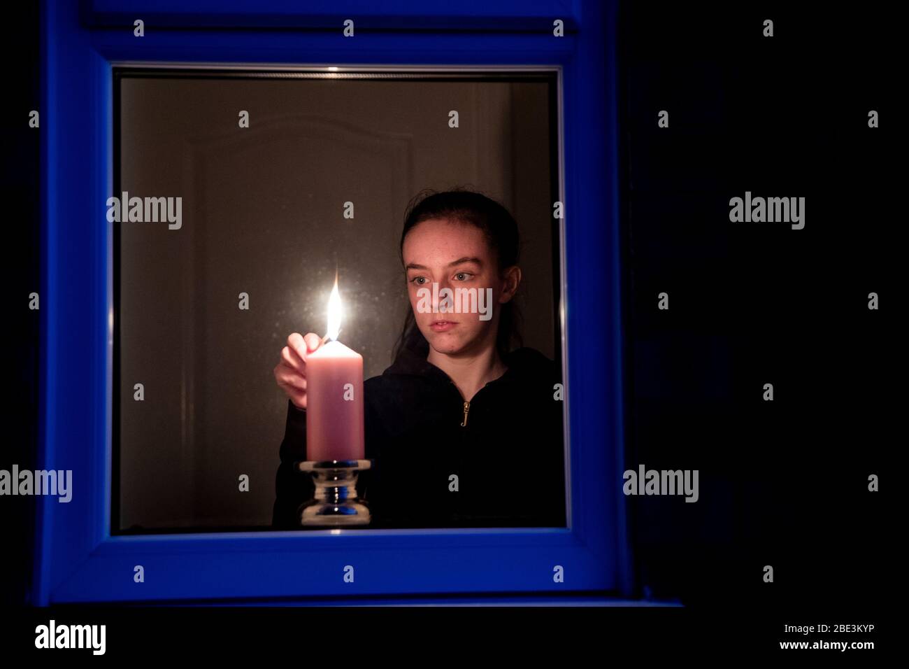 Maisy Byrne lights a candle in the window of a home in Liverpool after the Queen stressed the importance of maintaining the coronavirus lockdown during the Easter Bank Holiday weekend as she delivered what is believed to be her first Easter address. Stock Photo