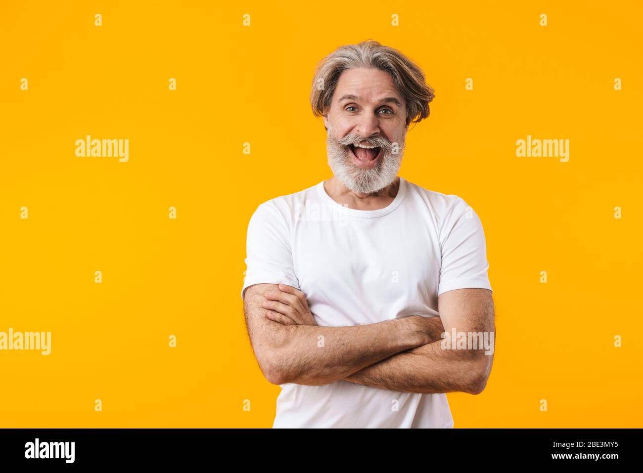 Image of cheerful positive senior grey-haired bearded man posing isolated over yellow wall background. Stock Photo