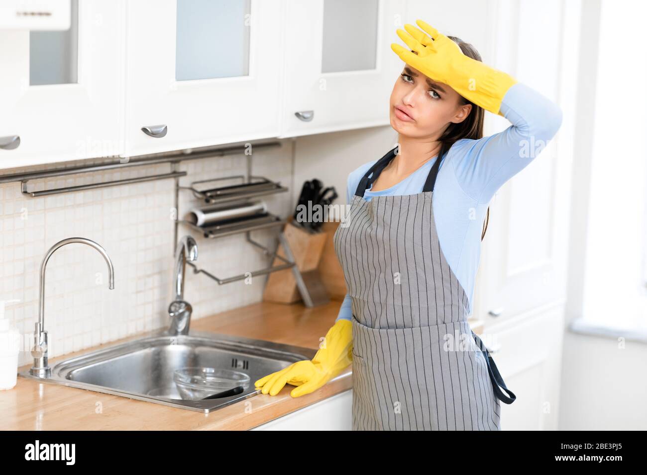 Tired woman wearing rubber gloves after washing dishes Stock Photo