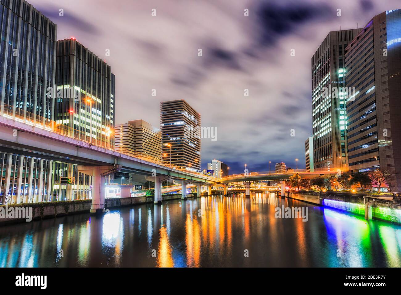 Dark river and highway bridges over water surface between high-rise towers in Osaka city at sunrise. Stock Photo