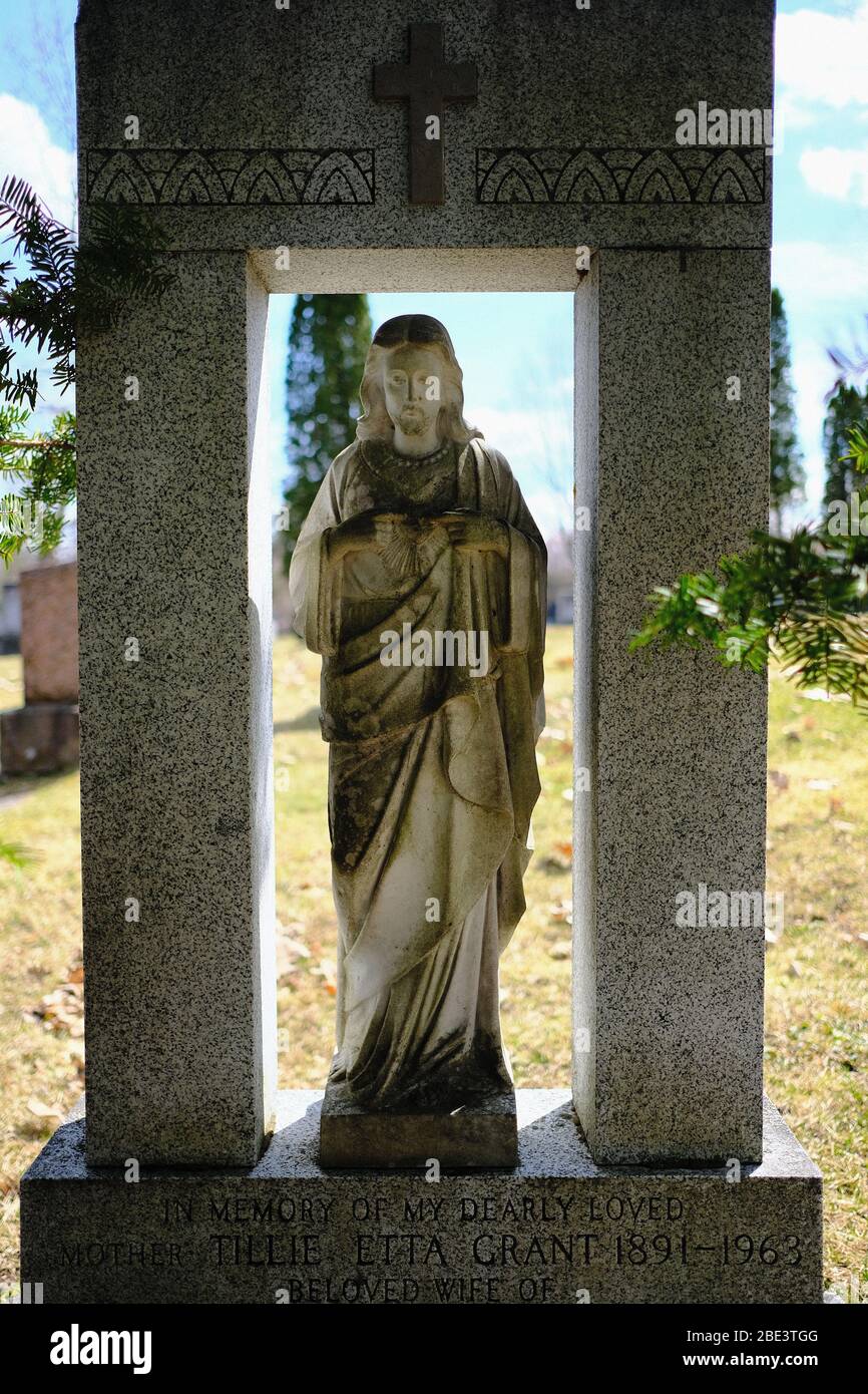 Statuette of Jesus in the shade of a pine tree, serving as a headstone at Beechwood Cemetery, Ottawa. Ontario, Canada. Stock Photo