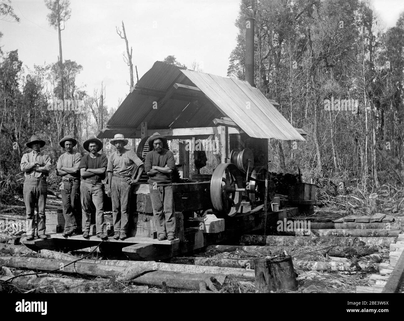 Men stand by their milling shed while clearning bush for the Main Trunk railyway line in the North Island of New Zealand, circa 1915, by photographer Albert Percy Godber Stock Photo