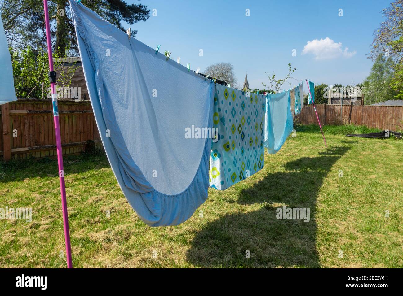 Bedding and sheets are freshly laundered and are hanging out to dry on a washing line in residential back garden. Stock Photo