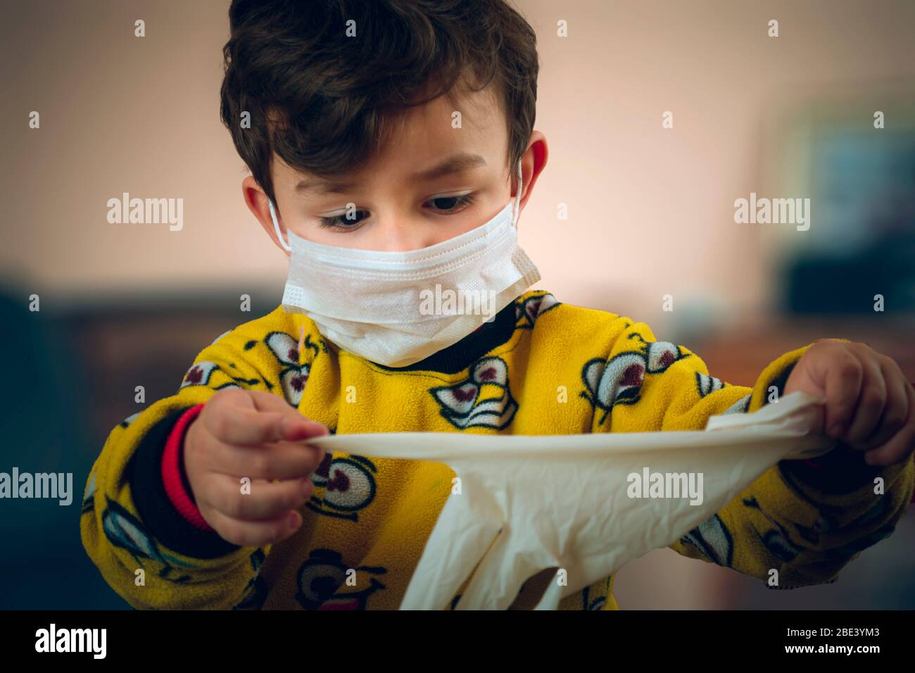 3 years old curious Turkish baby wearing pajamas and mask trying to wear surgical gloves Stock Photo