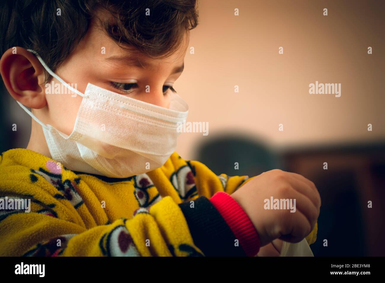 3 years old curious Turkish baby wearing pajamas and mask trying to wear surgical gloves Stock Photo