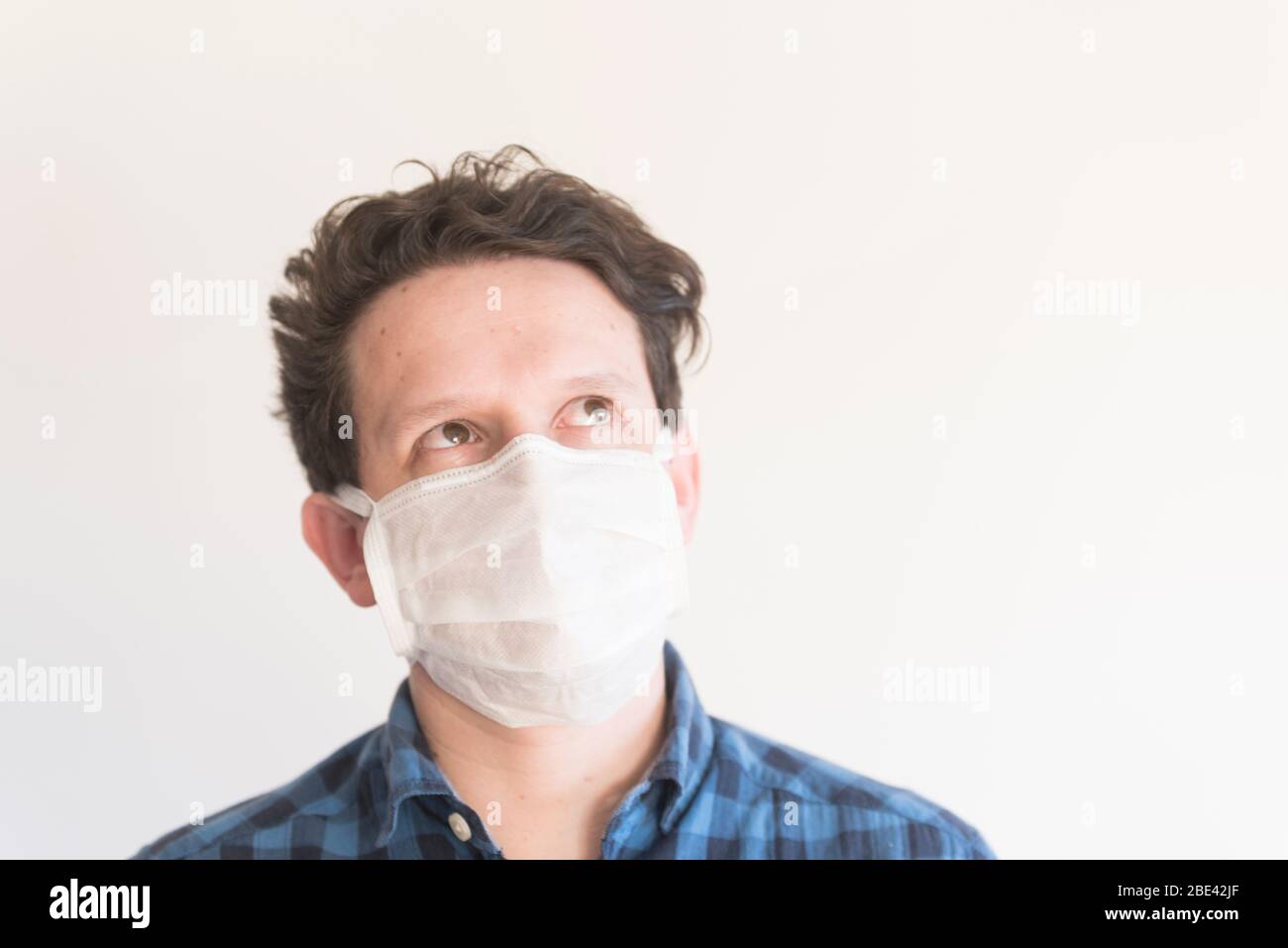 Frontal portrait of a young man looking up, wearing a disposable face ...