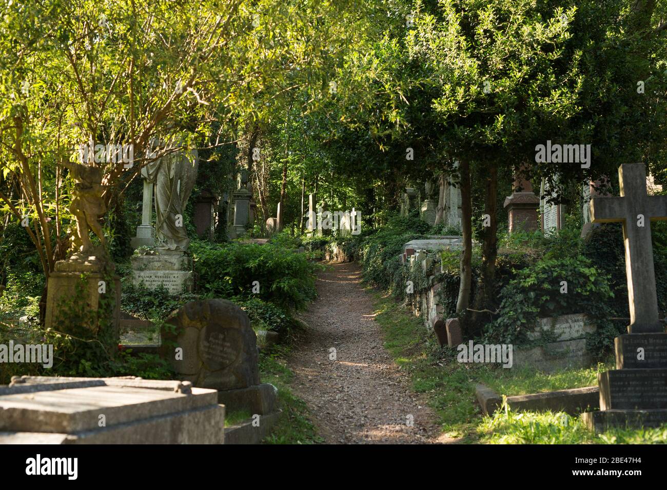 Sunlight filters through the trees over a walking path at Highgate Cemetery, London, England, United Kingdom. Stock Photo