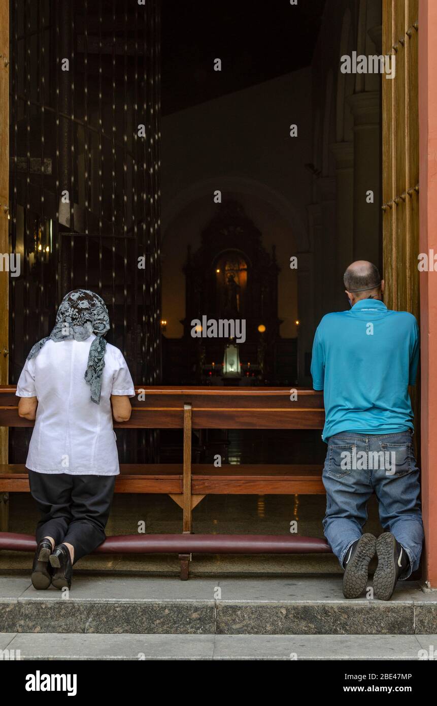 A man and a woman pray outside the door of a closed church in Caracas during an atypical Holy Week due to the quarantine by the Covid-19. Stock Photo