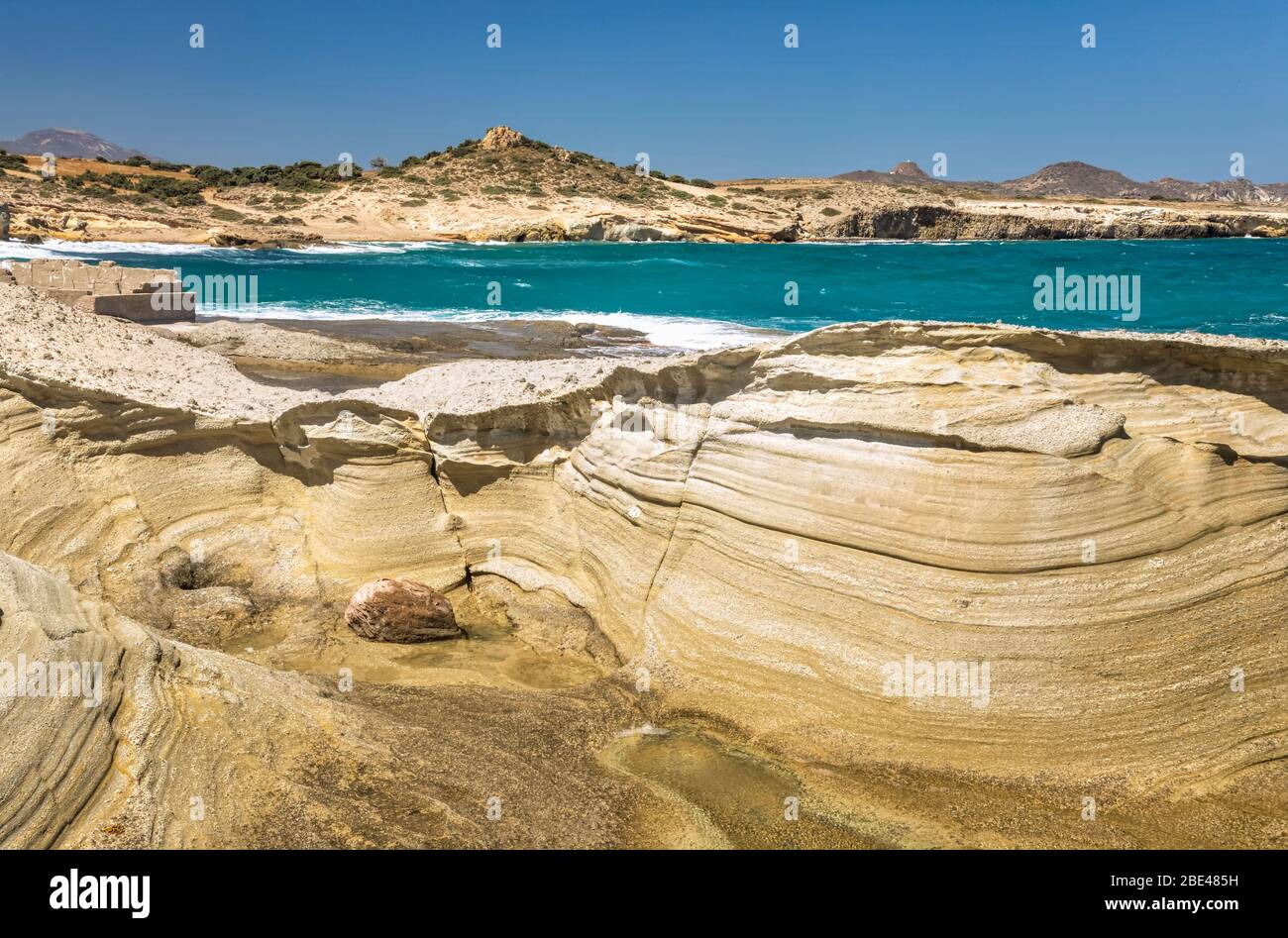 Eroded rock formations along the shore and turquoise ocean water along the coast of a greek island; Milos, Greece Stock Photo