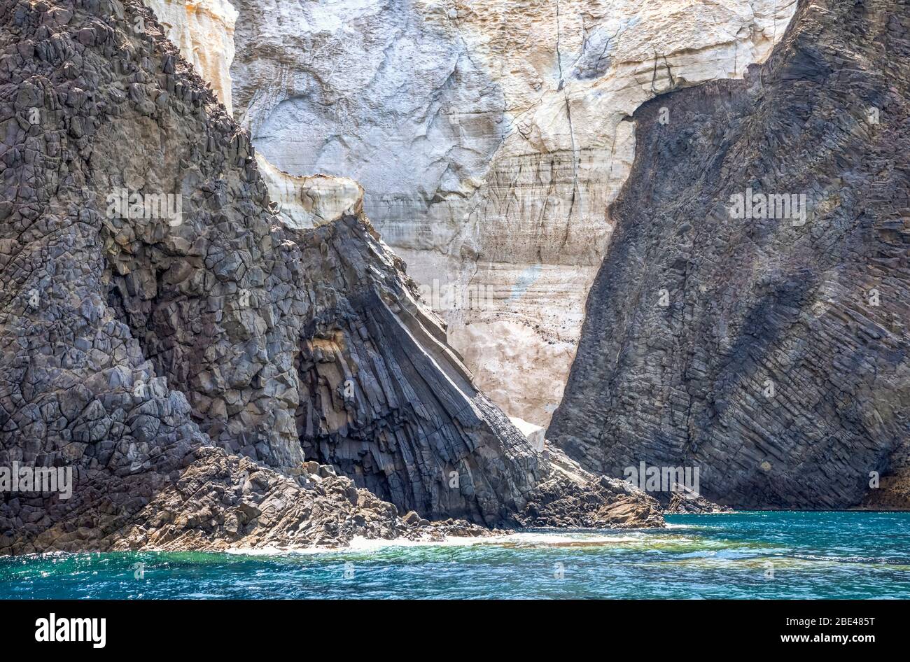 Rugged rock cliffs along the shore and turquoise ocean water along the coast of a greek island; Milos, Greece Stock Photo