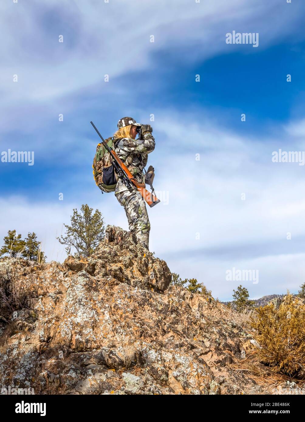 Hunter with camouflage clothing and rifle looking out with binoculars