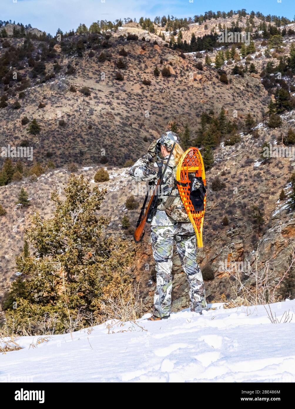 Hunter with camouflage clothing and rifle looking out with binoculars in winter; Denver, Colorado, United States of America Stock Photo