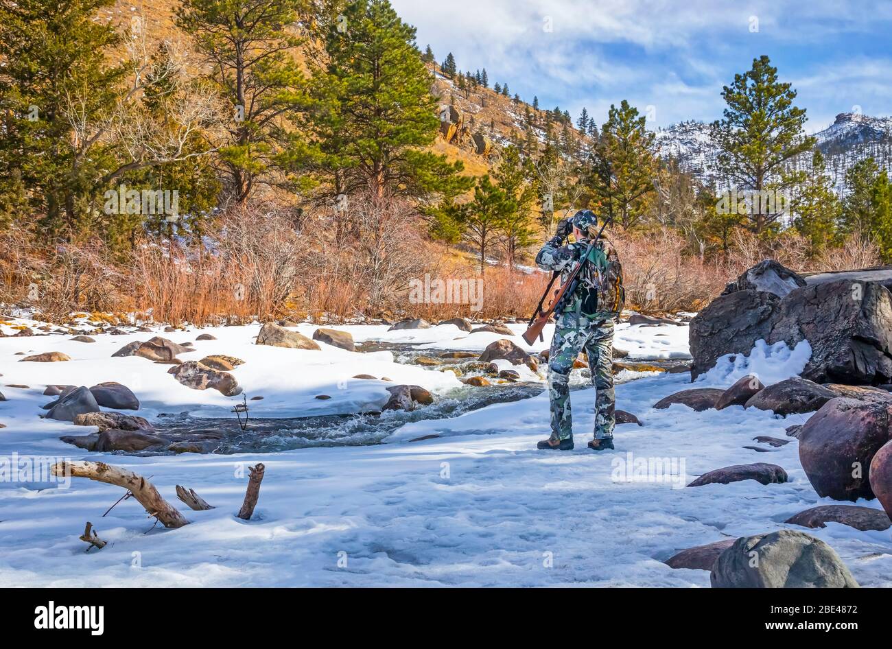 Hunter with camouflage clothing and rifle looking out with binoculars; Denver, Colorado, United States of America Stock Photo