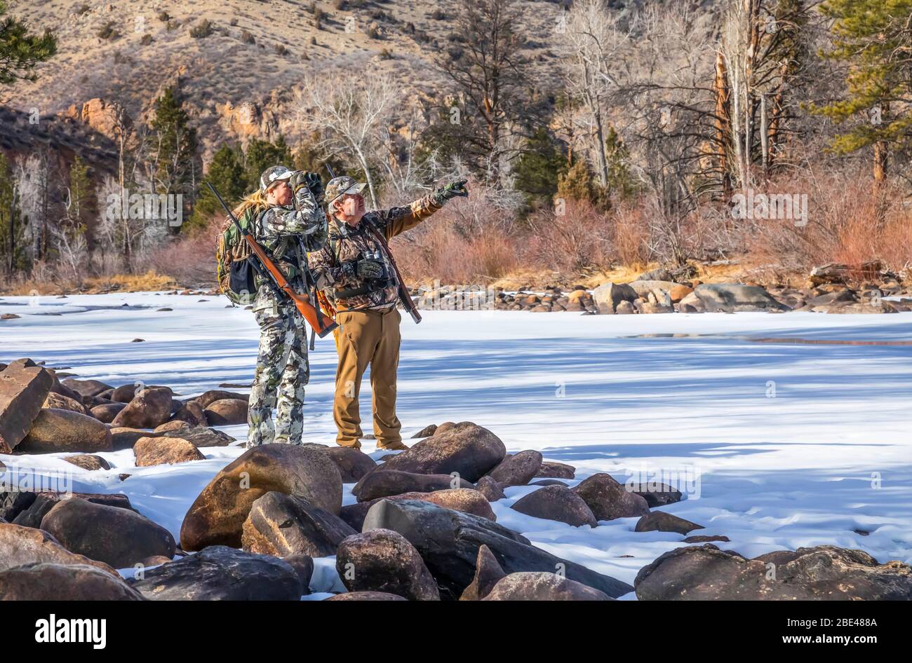 Hunters with camouflage clothing and rifle looking out with binoculars; Denver, Colorado, United States of America Stock Photo