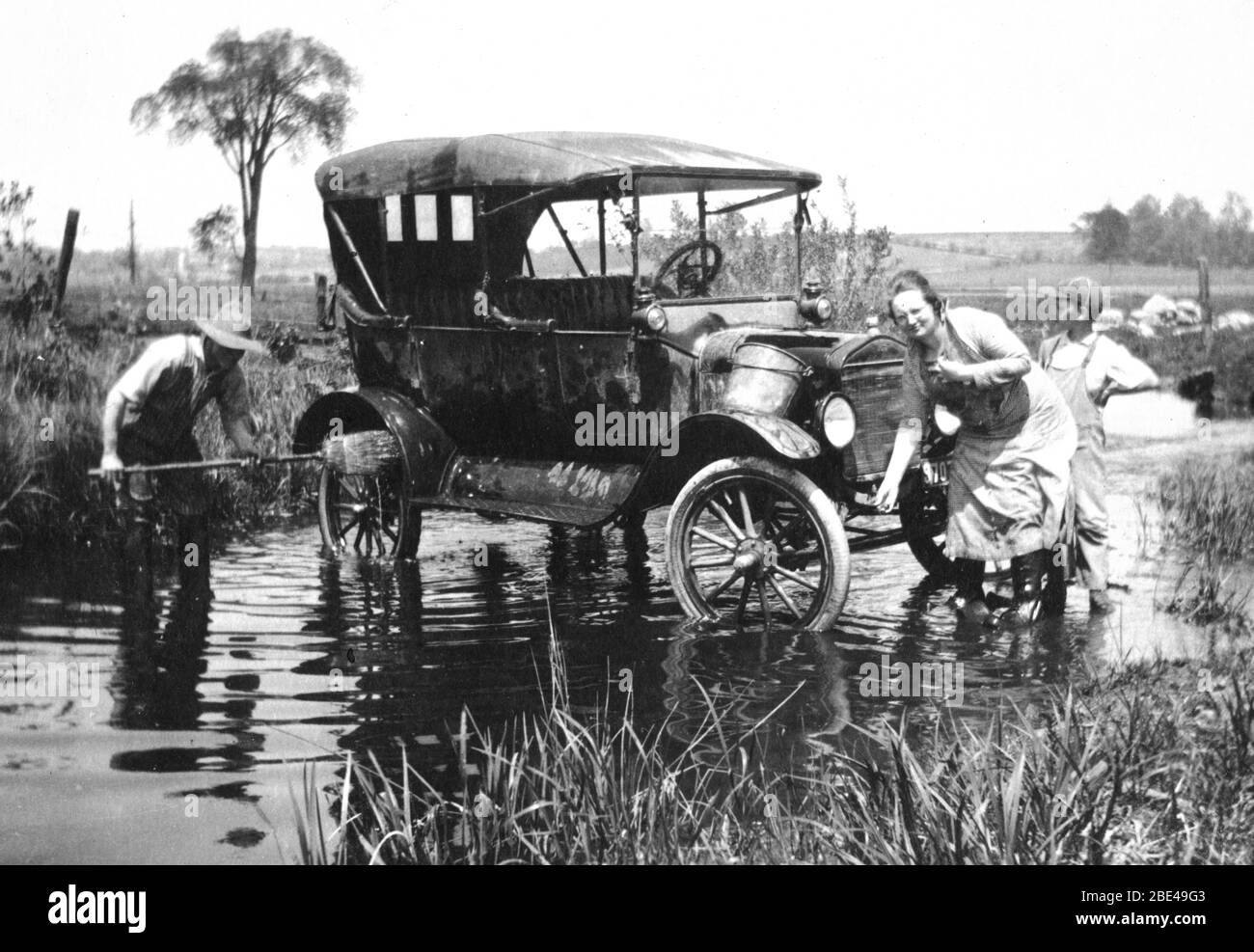 A farm family washing their car in a local creek, near Allenton, Wisconsin,  USA, in 1921. Dad uses a house broom to wash wheels while the lady works on  the front radiator