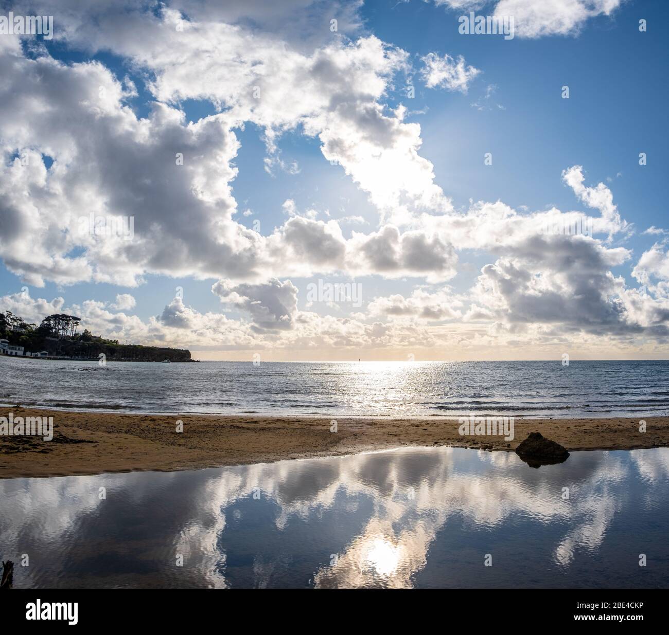 Sun shining through clouds and reflecting in the low tide sea water on the beach Stock Photo