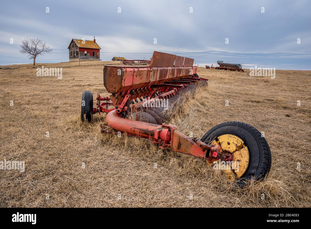 Vintage discer abandoned in a pasture with a weathered farmhouse on a hill in Saskatchewan Stock Photo