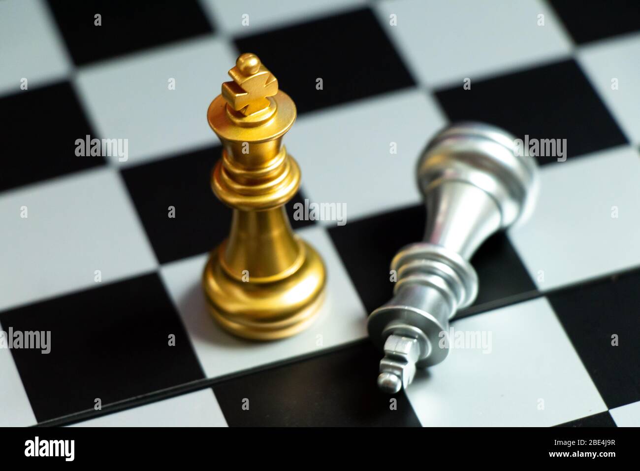 Gold king chess piece win over lying down pawn on black background