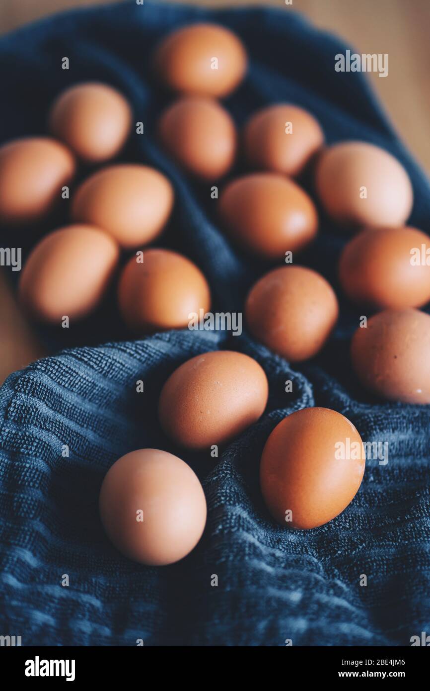 Brown fresh chicken eggs on blue kitchen towel. Pile of eggs on wooden table. Concept of farm products, natural food, easter. Protein food. Selective Stock Photo