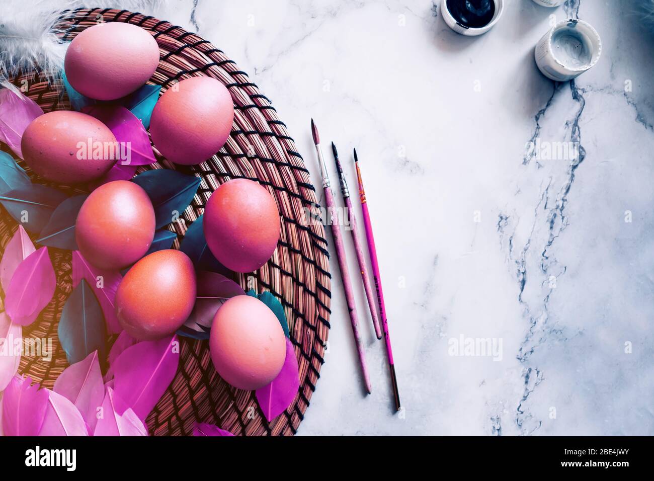 Colorful spring easter background with colored purple eggs, white feathers, dyes, brushes on light marble table. Copy space, top view. Happy Easter co Stock Photo
