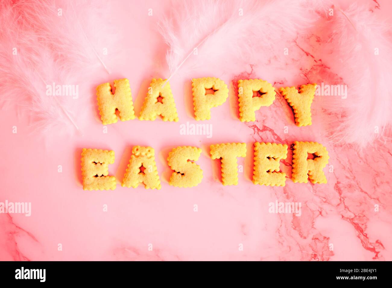 Top view of yellow eggs in carton boxes and on wicker kitchen stand, white feathers, lettering from cookies in shape of letters on marble table. Rusti Stock Photo