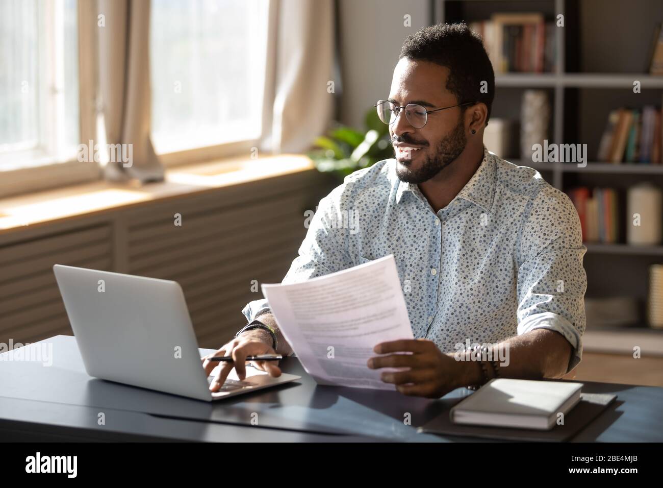 Happy millennial african american businessman in eyewear doing paperwork. Stock Photo