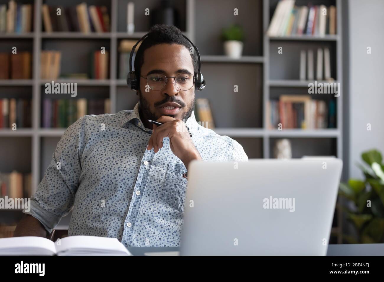 Focused millennial mixed race guy consulting clients online. Stock Photo