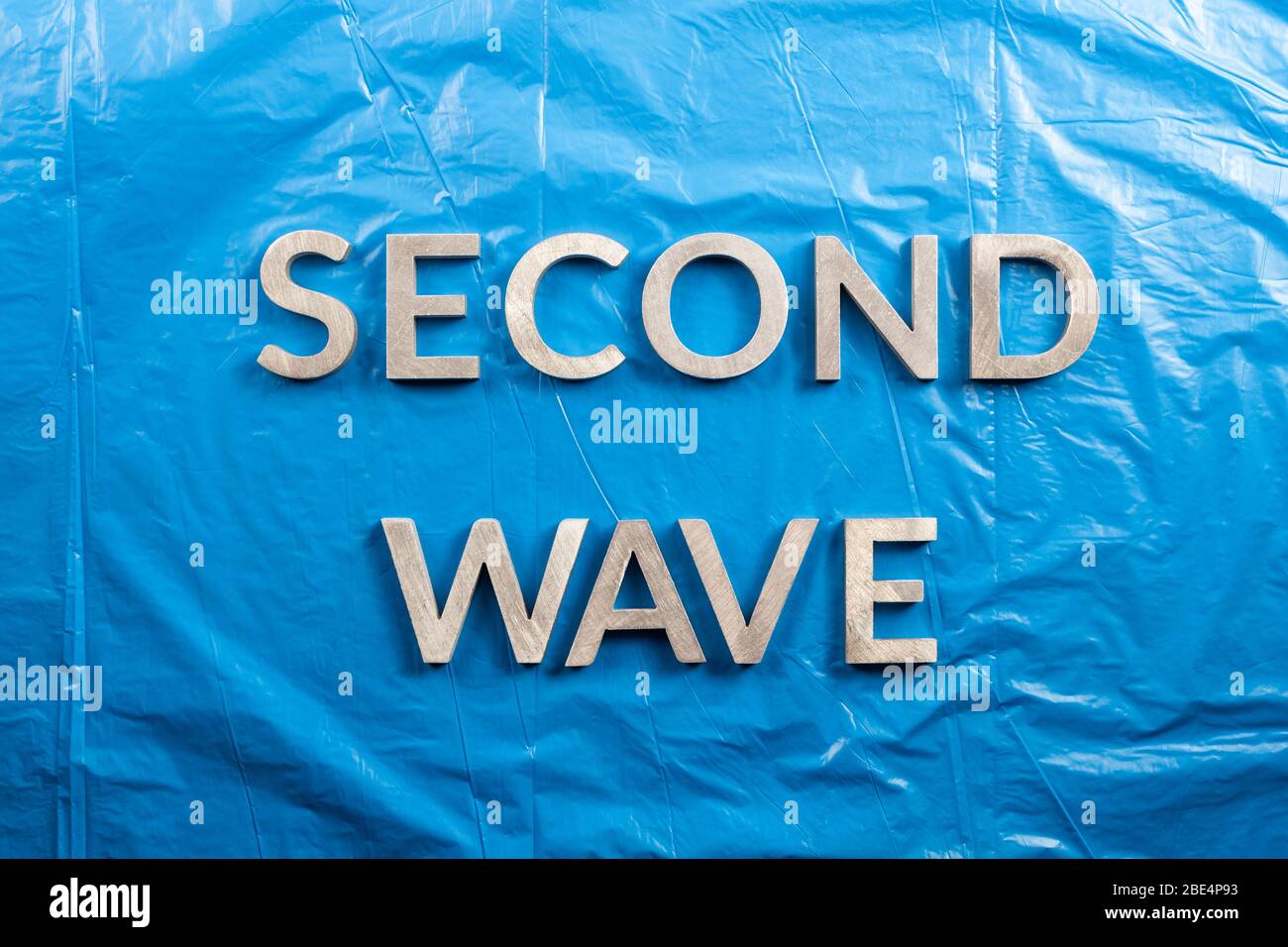 the words second wave laid with silver metal letters over crumpled blue plastic film background. Stock Photo