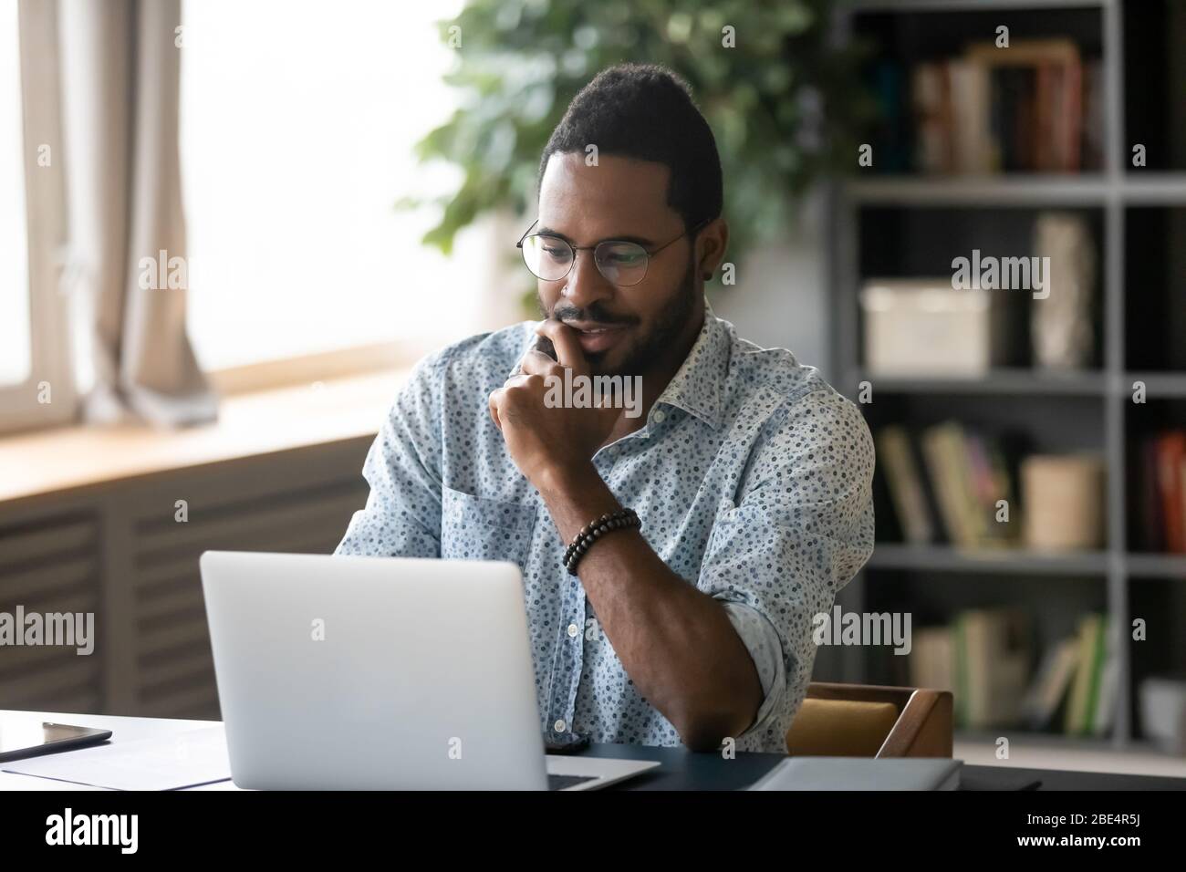 Smiling handsome young african american guy looking at computer screen. Stock Photo
