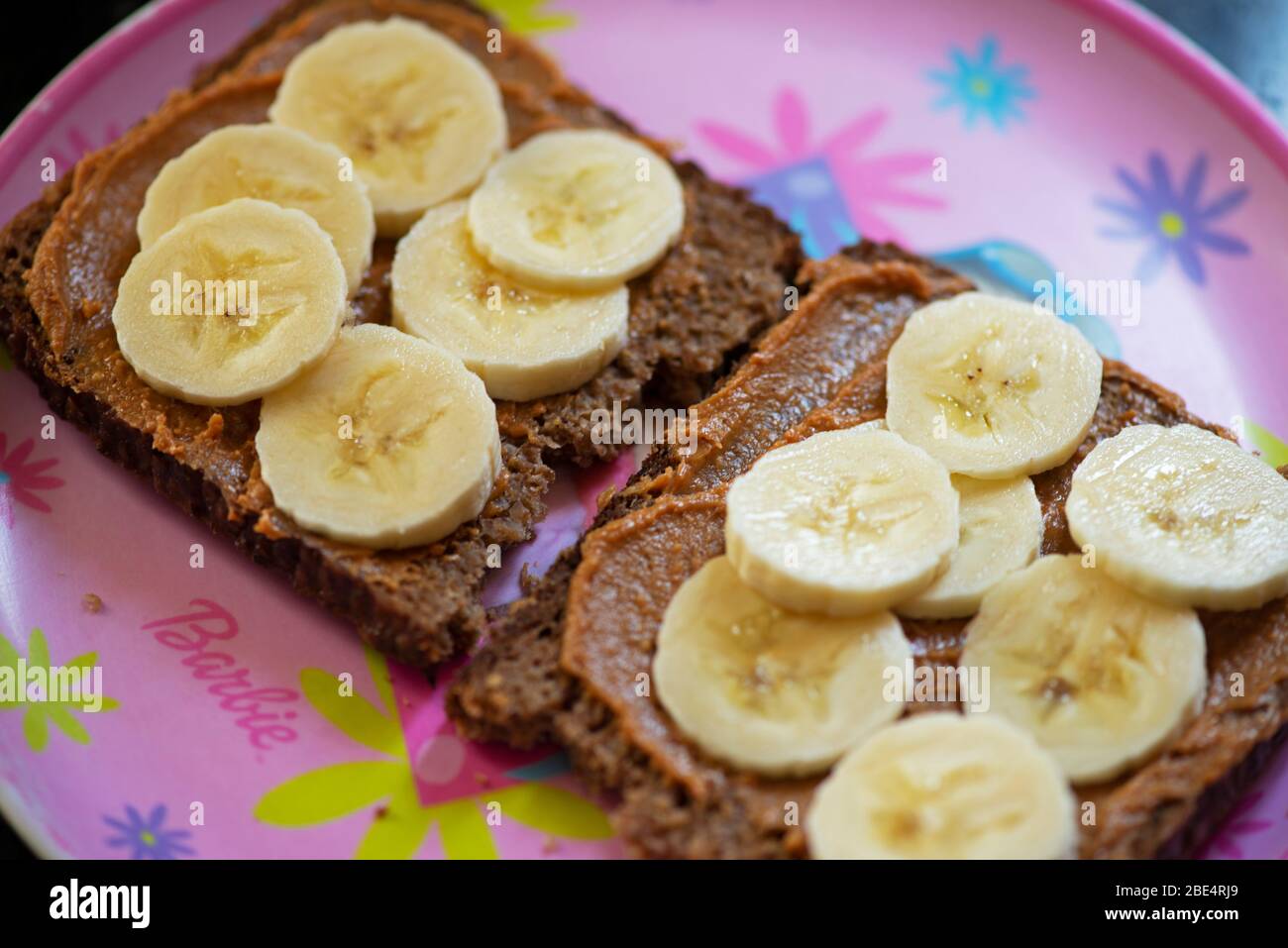 Slices of wholesome bread with peanut butter spread and banana slices on a girl's plate. Concept