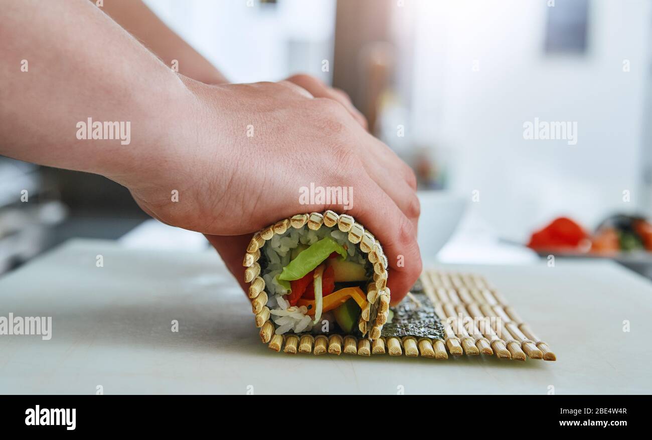 https://c8.alamy.com/comp/2BE4W4R/process-of-rolling-up-sushi-roll-with-vegetables-using-bamboo-mat-viewed-from-the-side-in-closeup-2BE4W4R.jpg