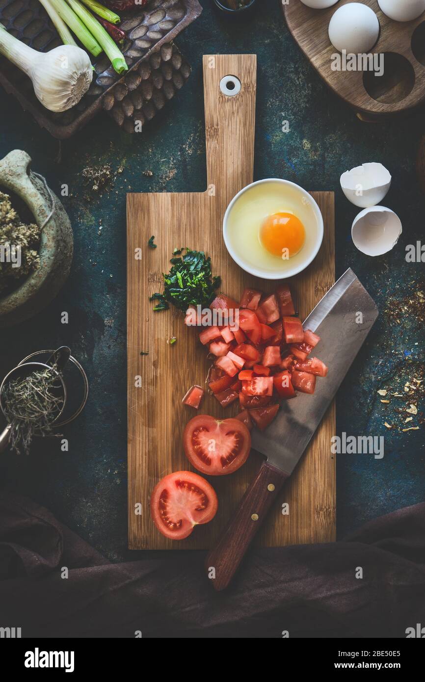 Tomatoes and eggs on wooden cutting board with knife on dark rustic kitchen table background. Shakshuka cooking ingredients. Top view. Healthy food ea Stock Photo