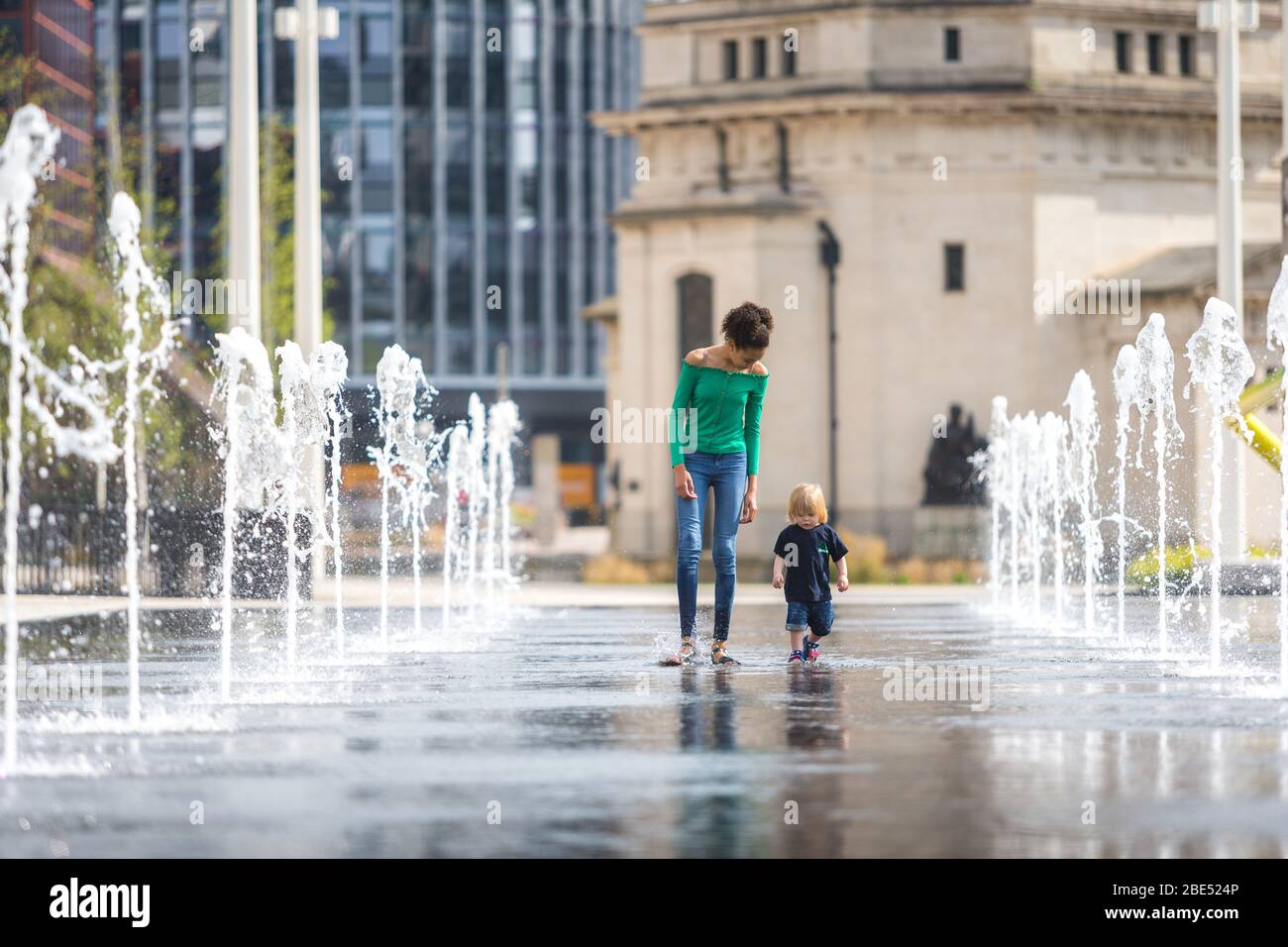 Birmingham, UK. 12th Apr, 2020. Twelve-year-old Mia takes her 18-month-old brother Jasper for their daily exercise walk through the fountains in Centenary Square, Birmingham city centre. Their family lives nearby. Easter Sunday has begun as a warm and sunny day. [Parental permission granted] Credit: Peter Lopeman/Alamy Live News Stock Photo
