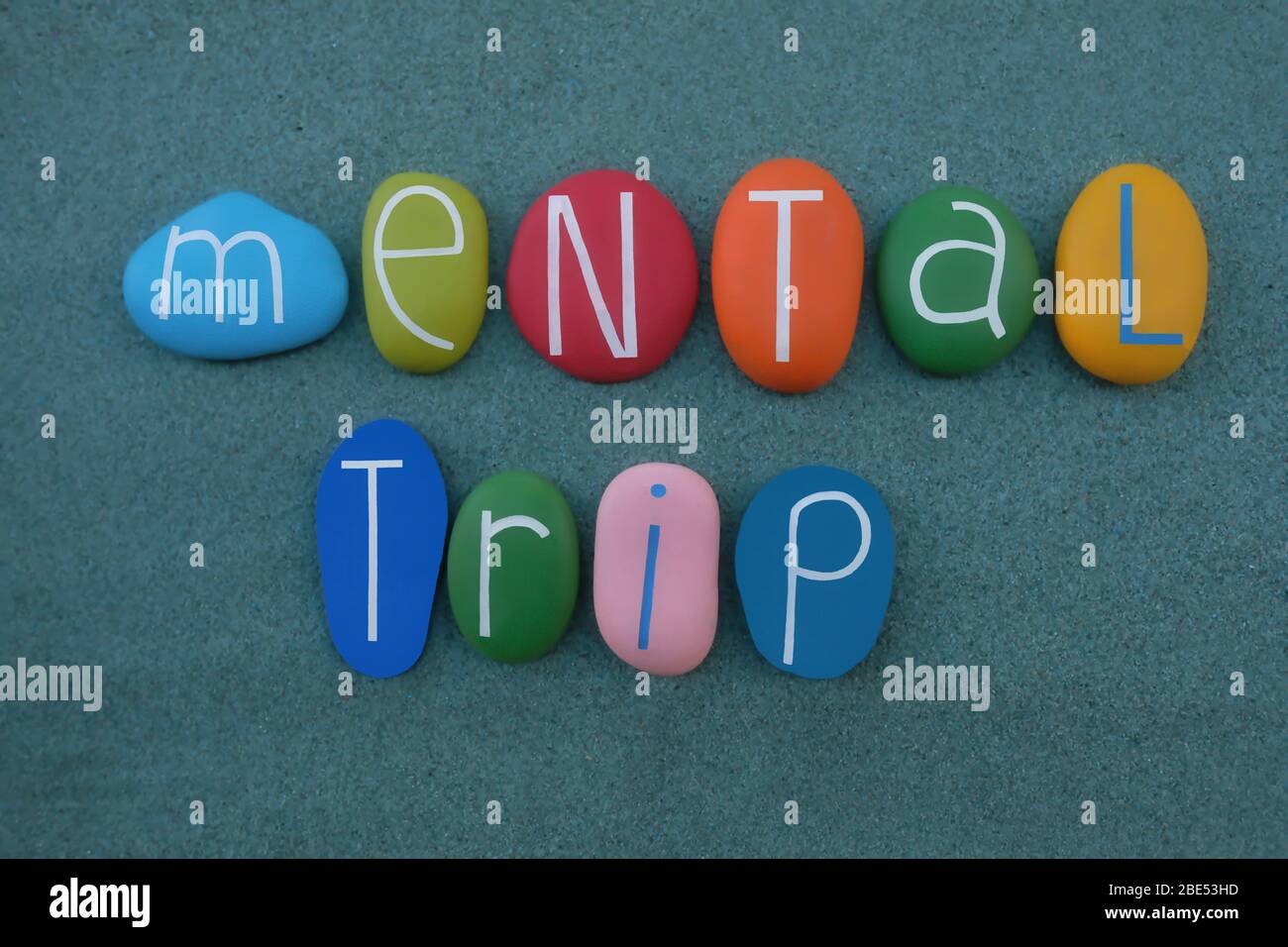 Mental trip text composed with multi colored stone letters over green sand Stock Photo