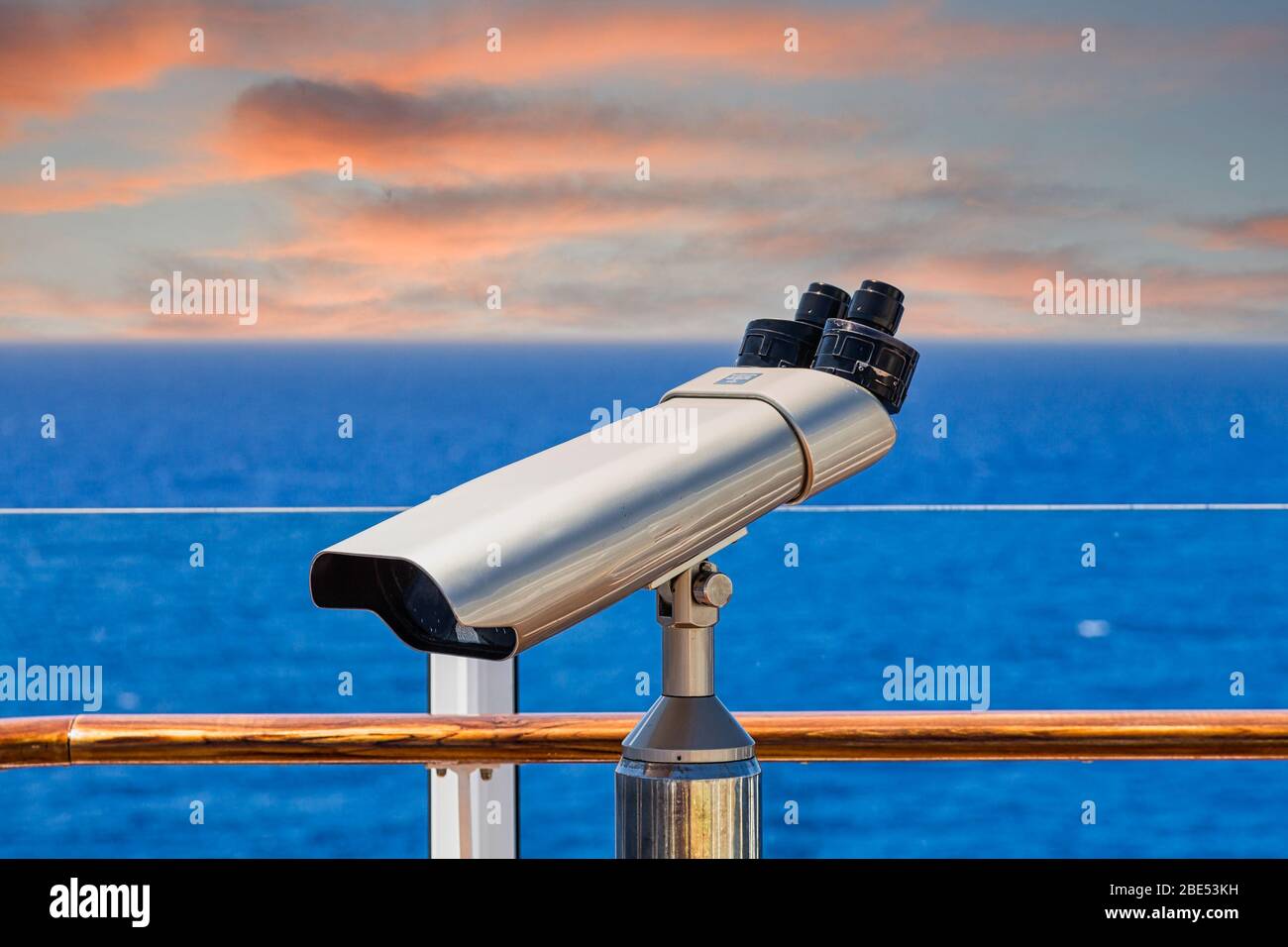 A silver spotting scope on the deck of a ship overlookng blue seas Stock Photo