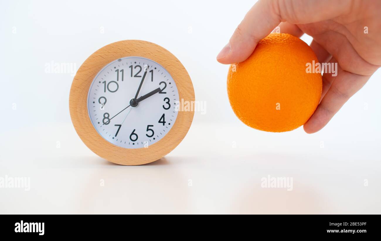 Alarm clock and orange fruit in hand on white table background Stock Photo