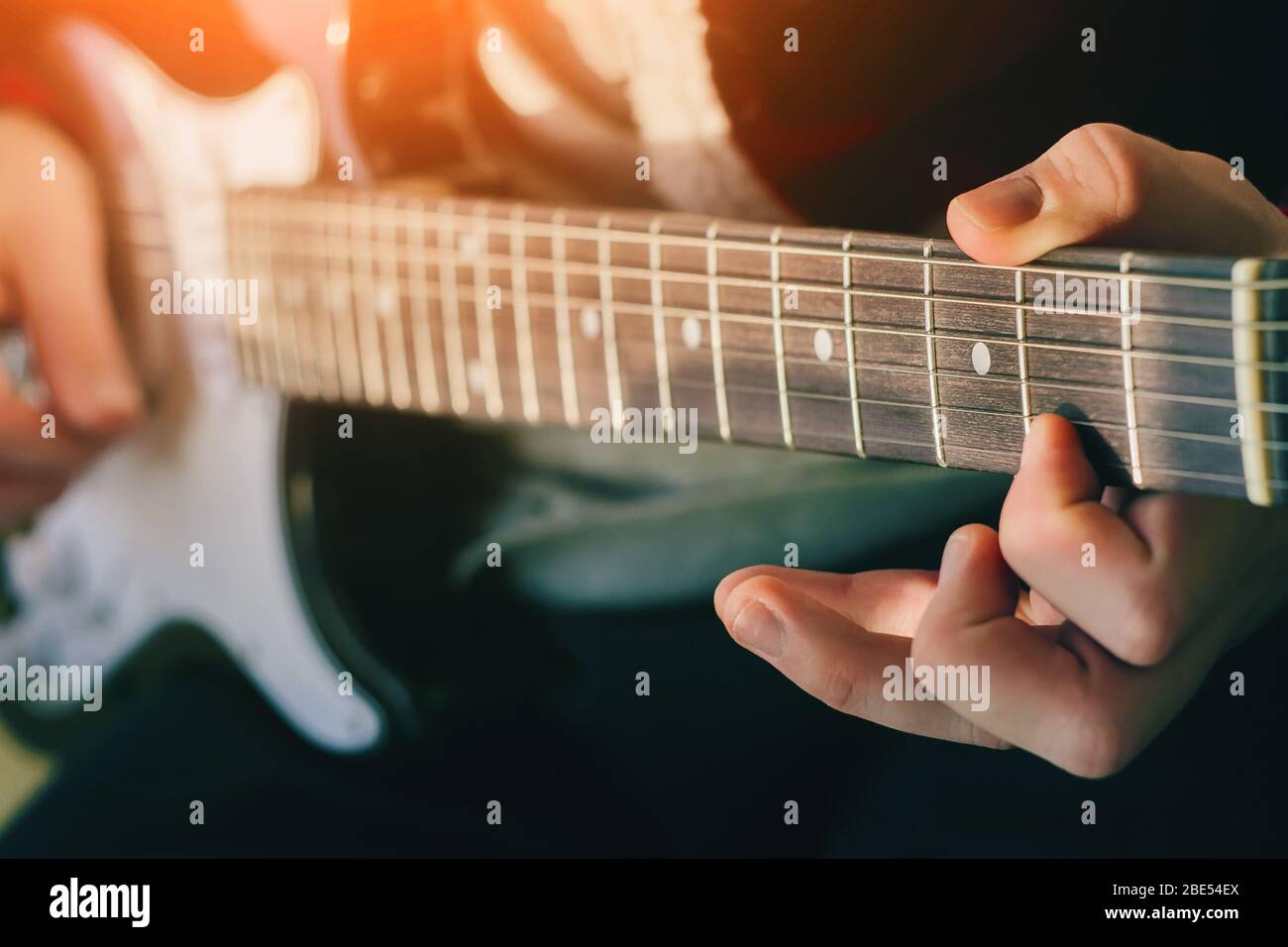 The musician plays an electric guitar, illuminated by bright sunlight, and holds the chords with