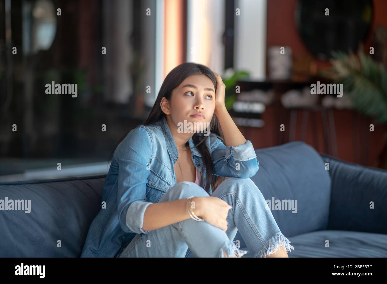 Sad young woman sitting on sofa, resting her head on her hand Stock ...