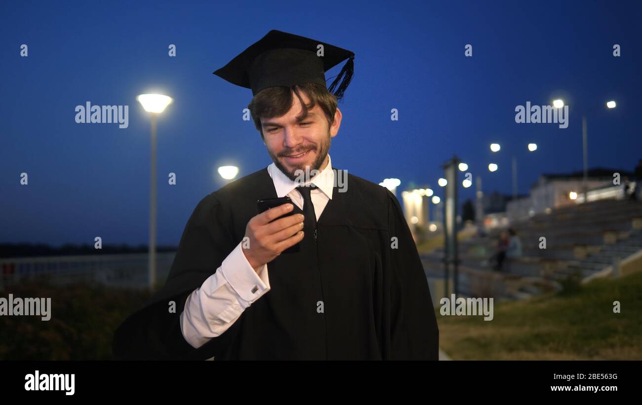 Graduate student walking in the evening and texting message on the phone. Stock Photo