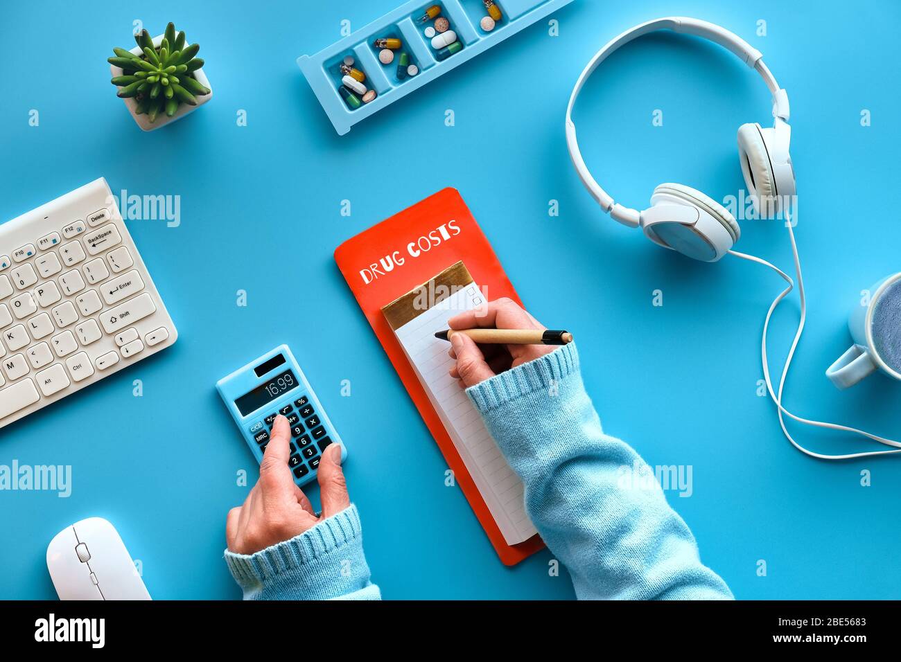 Creative flat lay with pen and calculator in hands to calculate drug costs. Keyboard, calculator, pills and pill case on mint blue background. Checkin Stock Photo