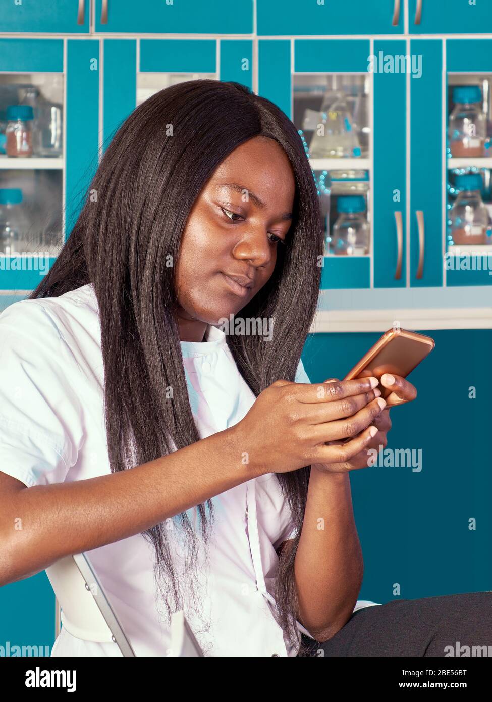 Young attractive African female scientist, graduate or medical student with mobile phone. The woman is smiling while using smartphone in scientific ch Stock Photo