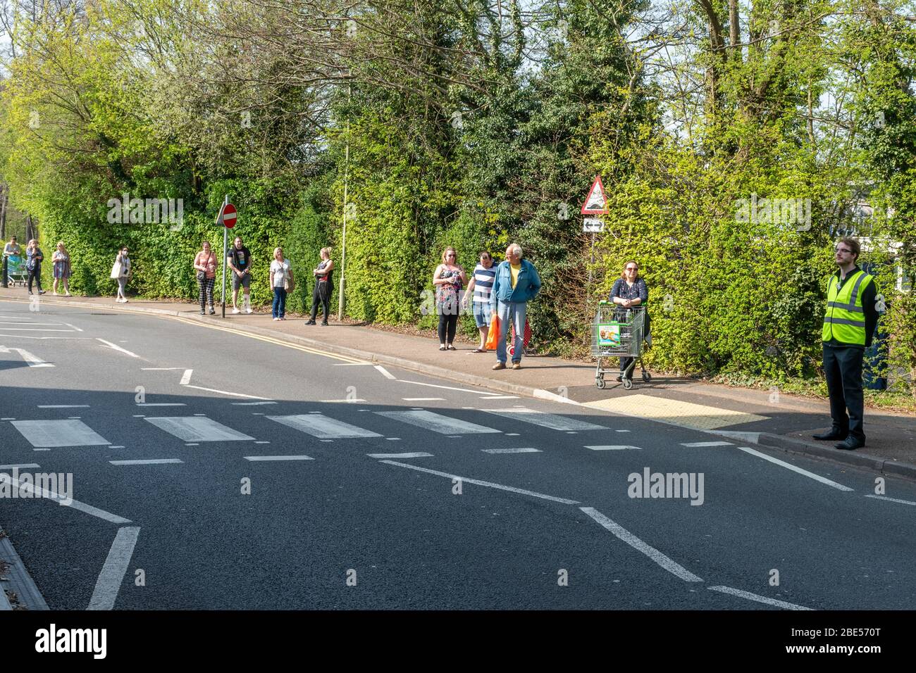 10 April 2020. During the 2020 coronavirus Covid-19 pandemic, a lockdown is in place in the UK, and people are only allowing to go out for specific reasons. including food shopping. A long queue to go into the Asda supermarket in Farnborough, Hampshire, to shop for essential supplies. People queuing are observing social distancing and standing about two metres apart. A member of staff helps to control the number of people entering the store on a 'one in and one out' basis. Stock Photo