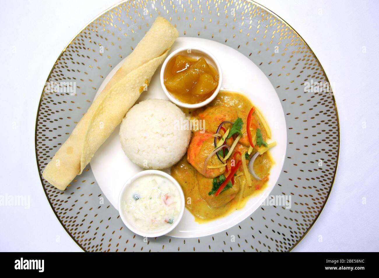 An Indian dinner ready to serve with chicken tikka masala, rice, chutney, raita, and a chapati bread, on a grey ornate plate & white table cloth. Stock Photo